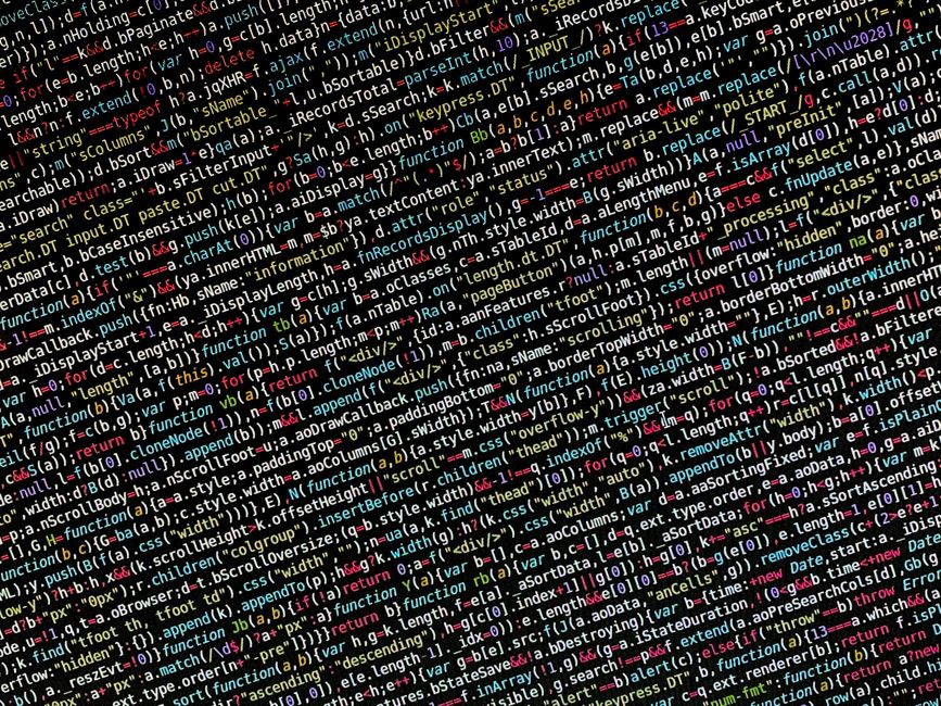 A close-up of a person's hands typing on a MacBook laptop displaying lines of code and programming interface, placed on a dark table. The background is slightly blurred, emphasizing the focus on the h