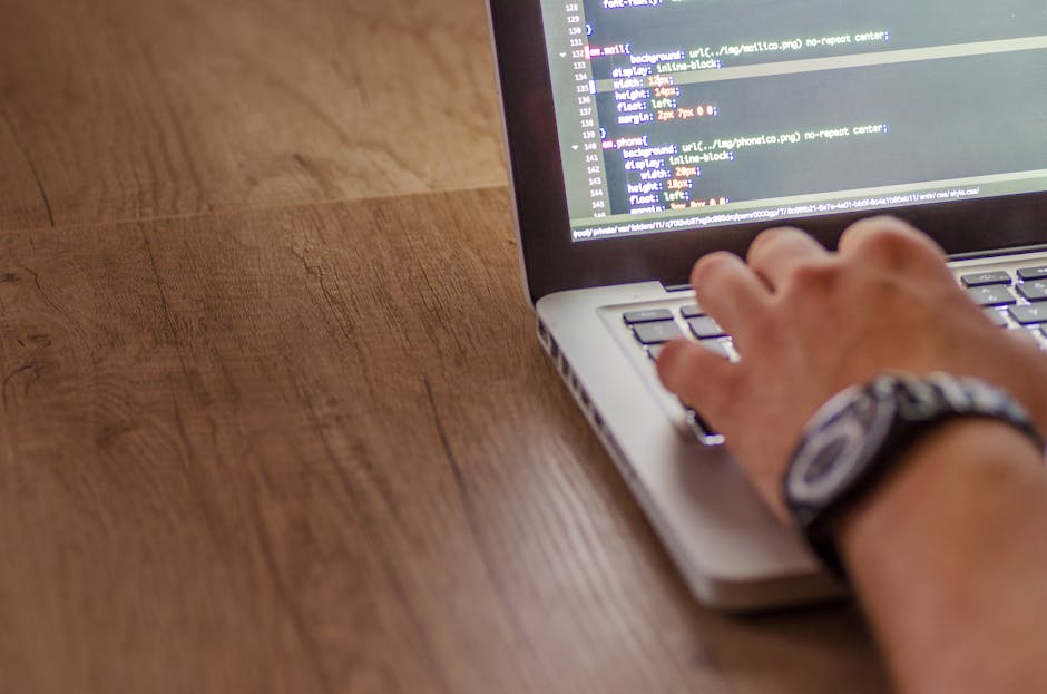 A close-up image showing a computer screen displaying lines of colorful code in red, green, purple, and blue text on a dark background, indicating programming or web development activity. The screen i